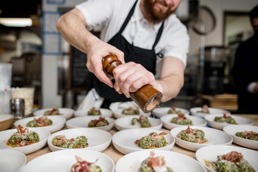 A chef seasoning a dish in a professional kitchen